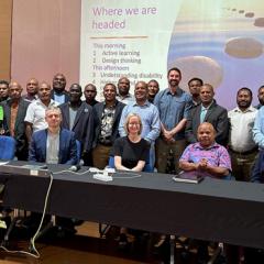 UQ Team with PNG colleagues at SILAG sitting at a long table and standing in front of project slides 