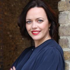 Claire leaning against brick wall looking to camera - wearing a formal and smart blouse